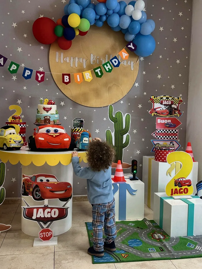 Un bambino davanti al tavolo della torta allestito a tema Cars