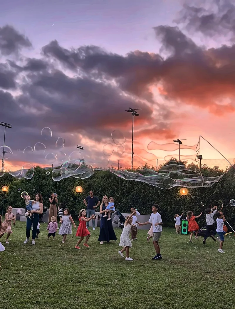 Bambini che inseguono bolle giganti sul prato, al tramonto