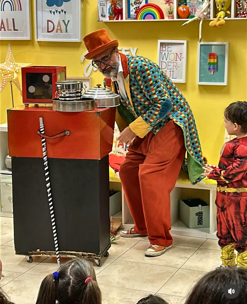 Il mago con cilindro arancione e giacca colorata fa il suo spettacolo davanti ai bambini