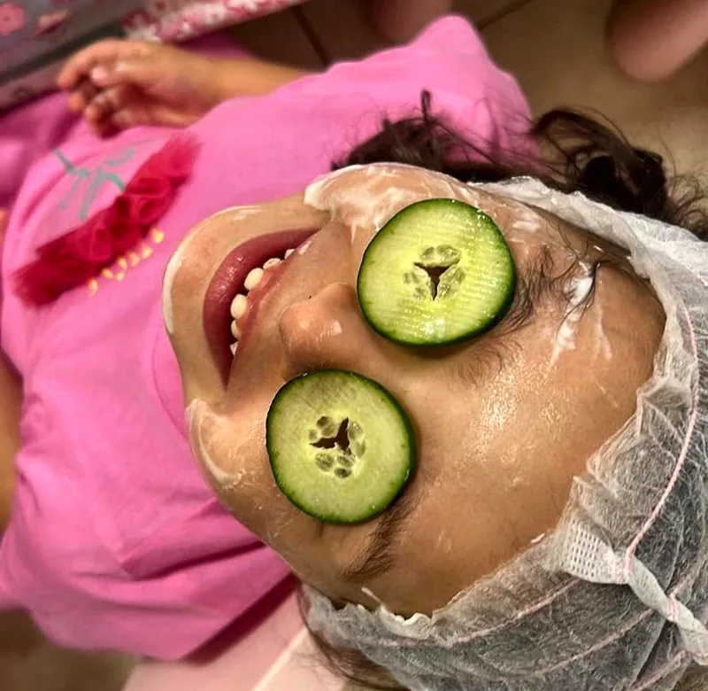 Una bambina con cuffietta, maschera viso e fette di cetriolo sugli occhi