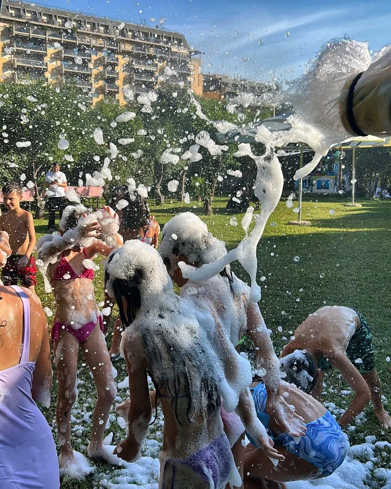 Bambini che giocano sul prato sotto gli spruzzi di schiuma