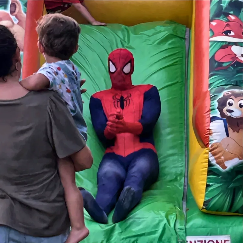 Un animatore vestito da Spider-Man scende dallo scivolo gonfiabile mentre un bambino lo guarda